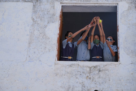 The Indian children with masks standing at the window and playing with a ball