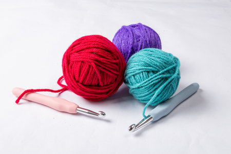 A closeup shot of red, purple, and blue knitting yarns and crochet hooks on a white surfaceの写真素材
