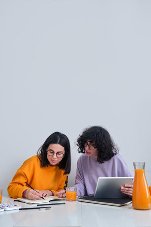 A view of two young women looking at something on the tablet on the table with fruits and juiceの写真素材