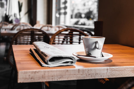 A closeup shot of a cup of coffee and a newspaper on the table in a cafeの写真素材