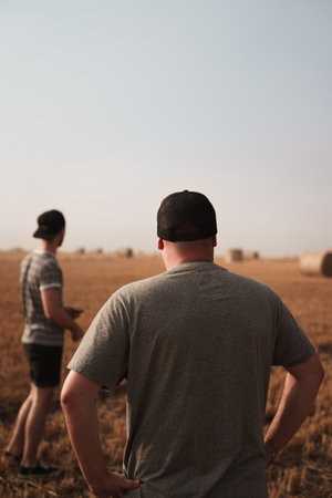 A back view of a male wearing a gray shirt and a hat standing on the field with his hands on his waistの写真素材