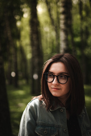 A shallow focus of a beautiful young brunette Ukrainian female wearing glasses in the woodsの写真素材