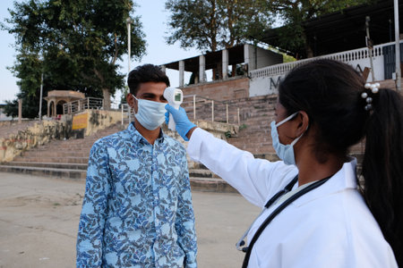 A medical worker monitoring the temperature of an Indian young man with a thermometer
