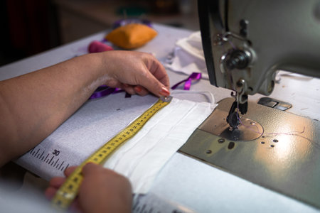 A closeup of a person measuring a facemask with a tape in the workshop