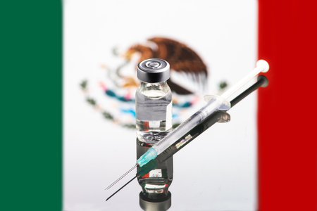 A syringe and a vaccine with the blurred background of the flag of Mexico on the backgroundの写真素材