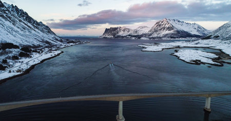 Aerial drone view of a boat driving under the Gimsoya bridge, colorful winter dusk. in Lofoten Norwayの写真素材
