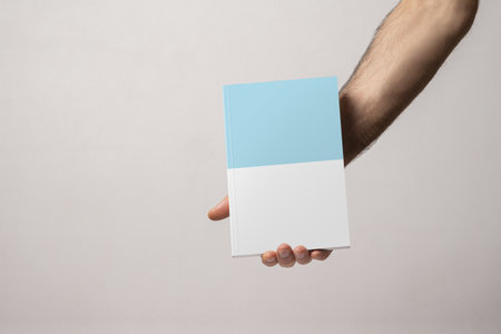 A male hand holding a closed book-catalog with blank coverの写真素材