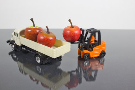 A closeup of a miniature figure of a worker in a forklift unloading the apples in a truckの写真素材