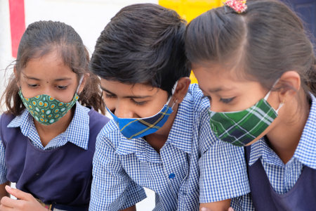 A group of Indian school children in face masks and uniforms using a tablet at school