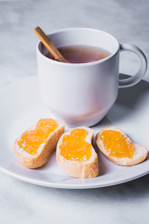 A yummy healthy breakfast - ceramic white plate in bright kitchen with honeyed bread and cup of teaの写真素材