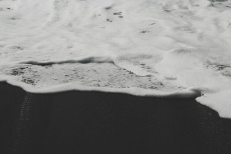 The foamy seawater and black sandy shoreの写真素材