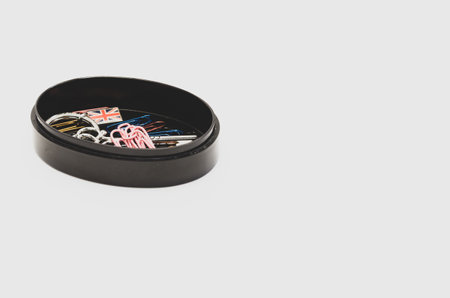 A closeup of paper clips and keychain on black container isolated on white background