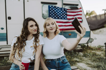 Spanish friends doing a selfie near a camp trailer with an American flagの写真素材