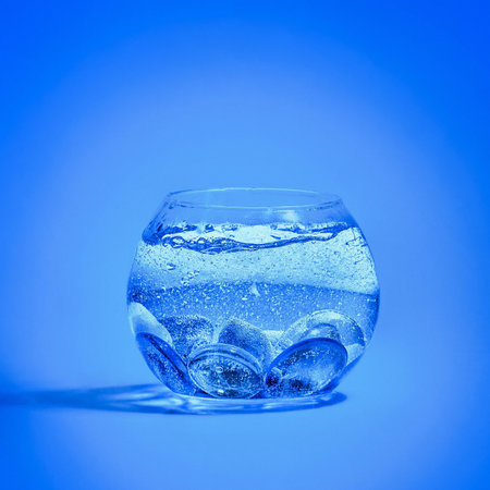 A closeup of a small aquarium filled with water with crystals in it against a blue backgroundの写真素材