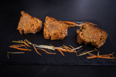 A closeup shot of slices of carrot cakes with carrots strips on a dark stone plate