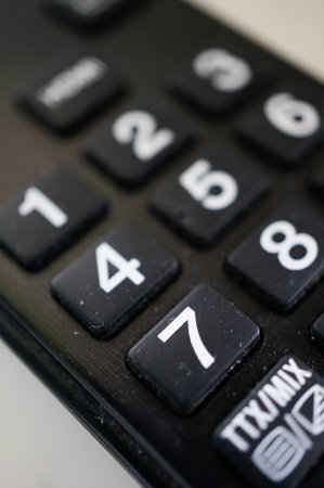 A vertical shot of a black remote control with buttons for a TV