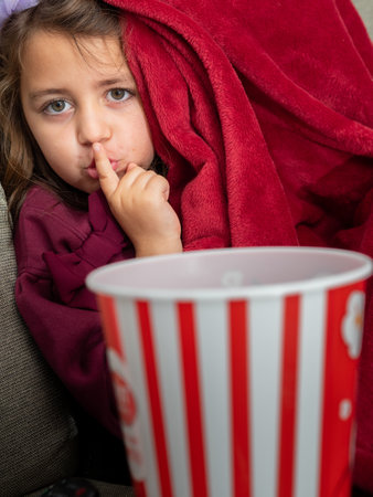 A Latina girl making the silent gesture with her finger, covering herself with a blanketの写真素材