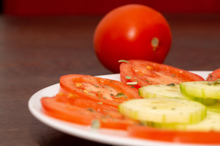 A plate of tomato and cucumber slices with whole fresh tomato on the sideの写真素材