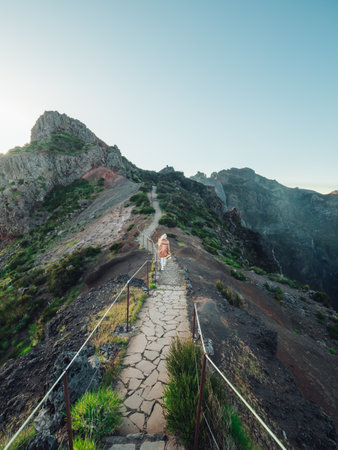 A vertical shot of a blonde woman hiking on a trail in the mountains, enjoying the beautiful viewの写真素材