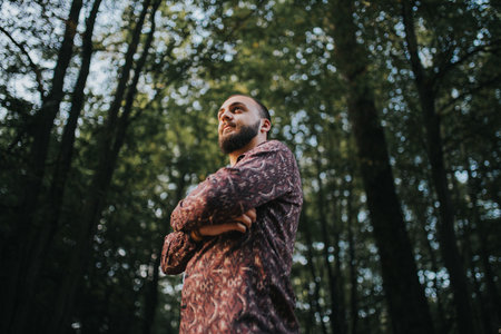 A low angle shot of a handsome Caucasian male posing with crossed arms in the woodsの写真素材