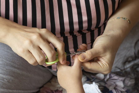 Young mother cutting child's fingernails by scissorの写真素材