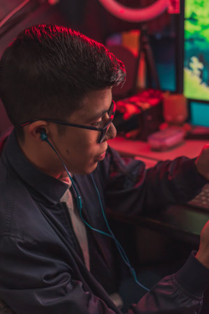 A vertical shot of a young gamer male wearing earphones and playing on his phoneの写真素材
