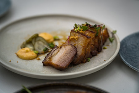 A closeup shot of pork dish garnished with fresh herbs and roasted garlic on a round plateの写真素材