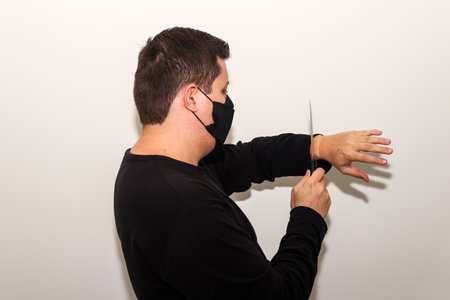 A male with a face mask cutting his hand with a knifeの写真素材