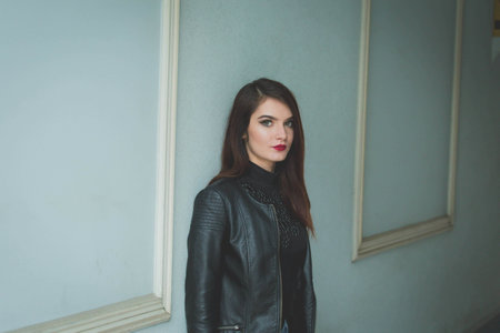 A young brunette female in a leather jacket posing in front of a wal
