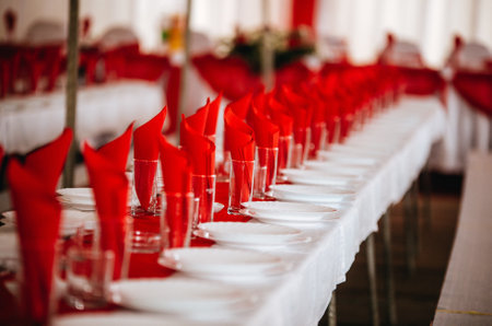 A red-themed wedding table decoration with red napkins and empty glassesの写真素材