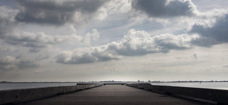 A panoramic shot of a pier on the sea under a cloudy sky and sunlight - great for wallpapersの写真素材