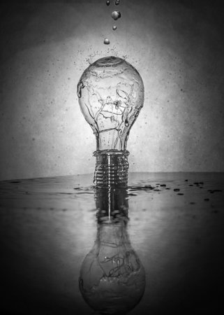 A vertical grayscale shot of a light bulb with water dropletsの写真素材