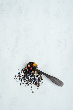 A top view vertical shot of a spoon full of black tea mixed with flower petals on a light background with copy space.の写真素材