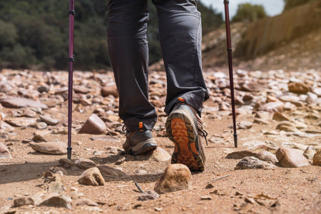 Man hiking along stone path with hiking shoes and walking poles. Man hiking on sand and stones path near mountains. Copy spaceの写真素材
