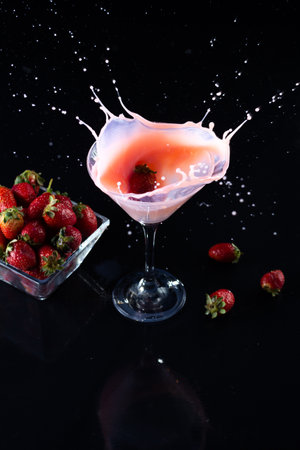 A vertical shot of smoothie in a glass and a small bowl with strawberries on a dark backgroundの写真素材