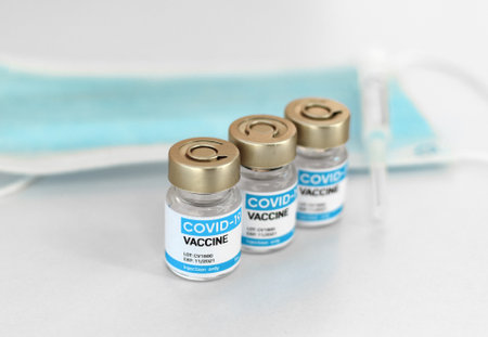 Close-up selective focus image of generic brand covid vaccine vials, mask and syringe on white...