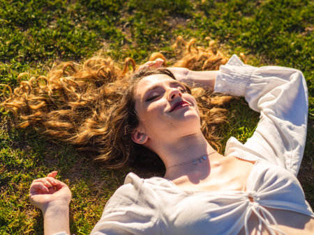 A pretty Spanish female is relaxing on the grass with eyes closed and long hair spread out on the grassの写真素材