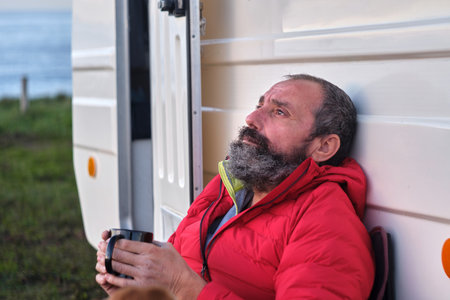 A cool bearded Spanish man holding a mug of hot drink and enjoying his time next to a caravanの写真素材
