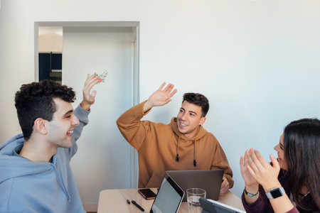 The three friends working together at home. Happy men giving a high-five while the female looks at themの写真素材