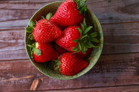 A top view of juicy fresh strawberries in a green bowl on a wooden surface
