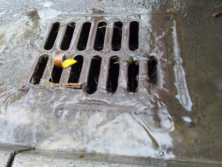 A closeup of a storm drain in the ground with soap and water going down its rectangular holes