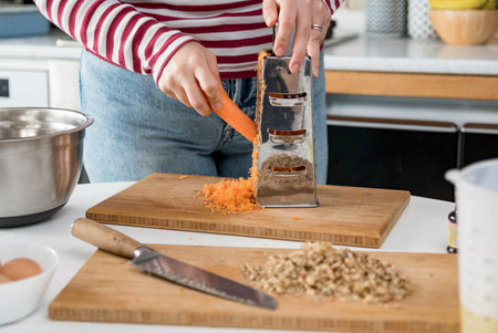 A closeup of female hands grating a carrot in the kitchen
