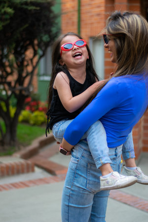 An adorable Latin mother and daughter in sunglasses walking through the city and having funの写真素材