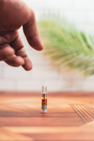 A hand reaches to pick up a cannabis vaporizer cartridge from a counter at home.