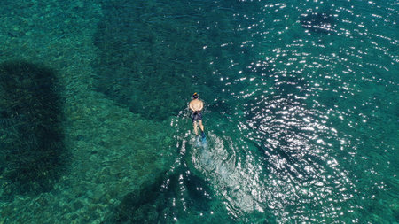 An aerial view of a man swimming in the wavy ocean gleaming under the sunrays on the coastの写真素材