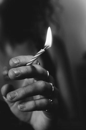 A grayscale shallow focus shot of a female hand holding a lit birthday candle as a cigaretteの写真素材