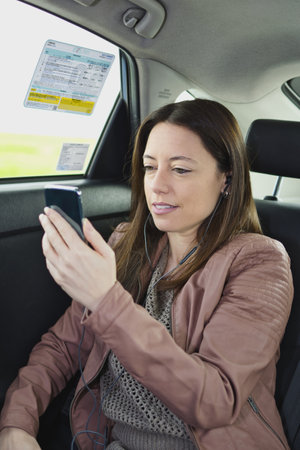 A female customer using her smartphone with a headset on a taxi