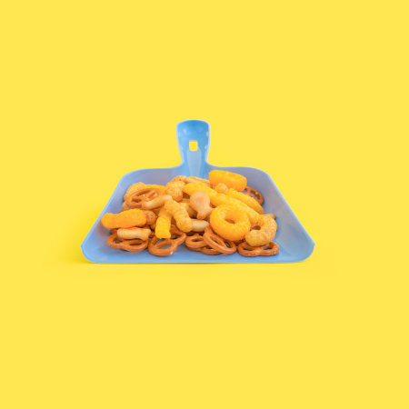 A creative junk food concept with a dustpan and snacks on yellow backgroundの写真素材