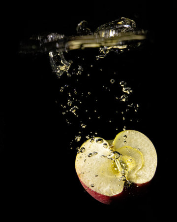 A vertical shot of a sliced apple dropping into water on a black backgroundの写真素材