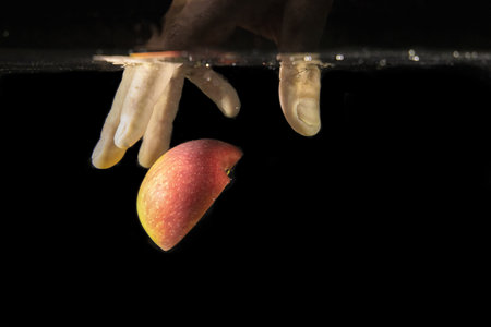 A closeup shot of a hand reaching for an apple in the water on a black backgroundの写真素材